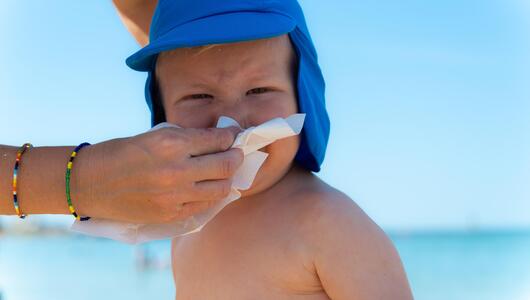Mutter putzt Kind am Strand die Nase