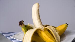 Eine teilweise geschälte Banane liegt auf mehreren ungeschälten Bananen, die auf einem weissen ...