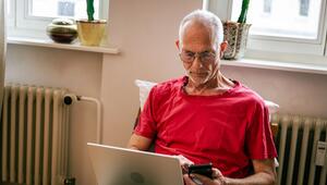 Ein Senior sitzt mit Laptop und Smartphone auf einem Sessel