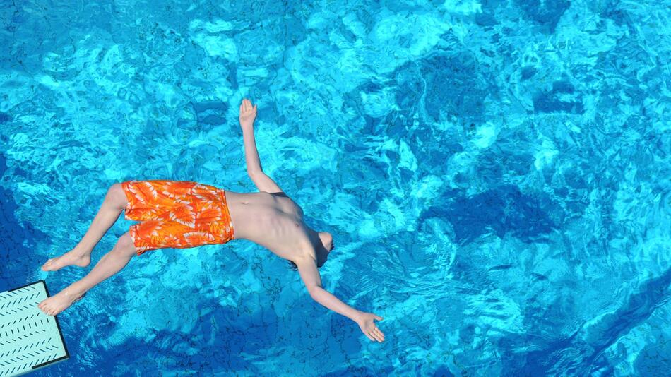 Junge springt vom Strungbrett in das Becken eines Freibads