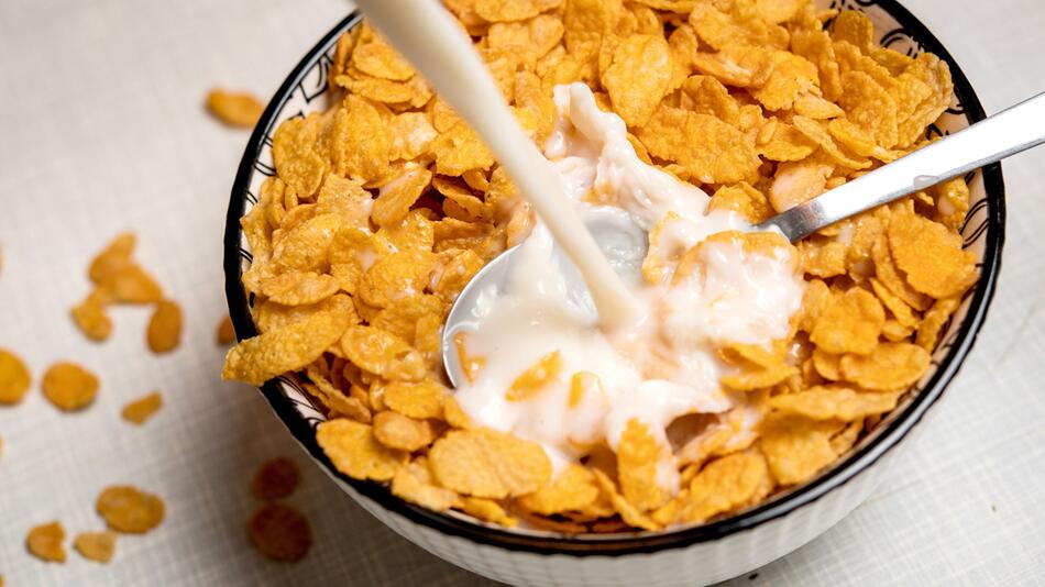 Milch wird in eine Schale Cornflakes gegossen