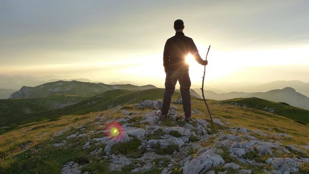 Wanderer geniesst bei Sonnenuntergang die Aussicht über die Berge