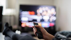 Eine Frau sitzt vor dem Fernseher und hält die Fernbedienung