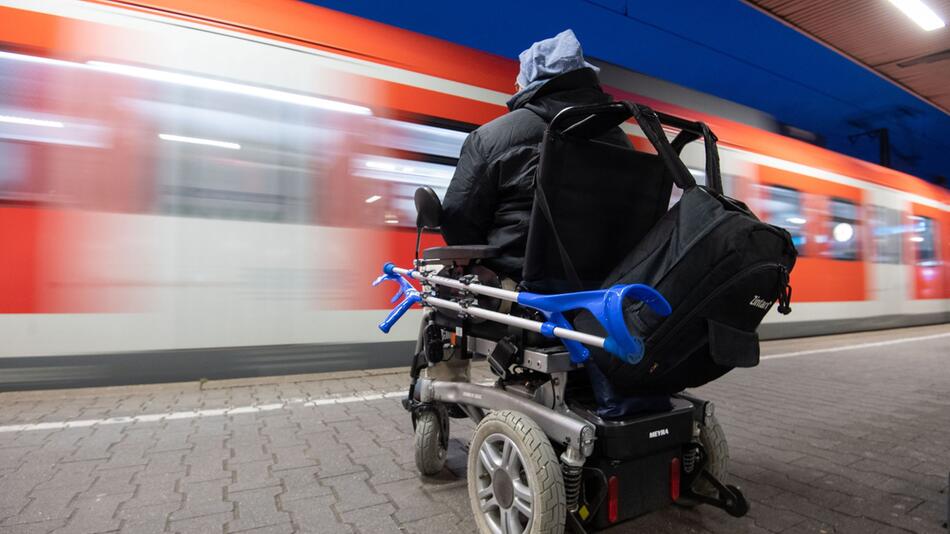 Mann im Rollstuhl steht am Bahnhof an einem Gleis