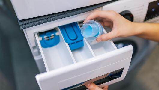 Frau gibt Waschmittel in ein offen stehendes Waschmittelfach 