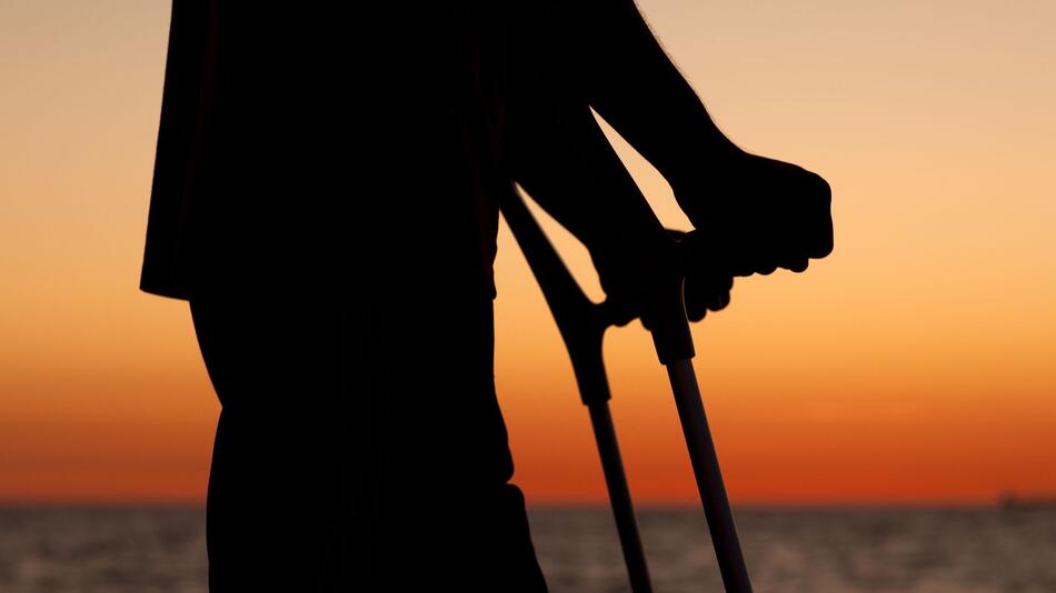 Ein Mann mit Krücken bei Sonnenuntergang