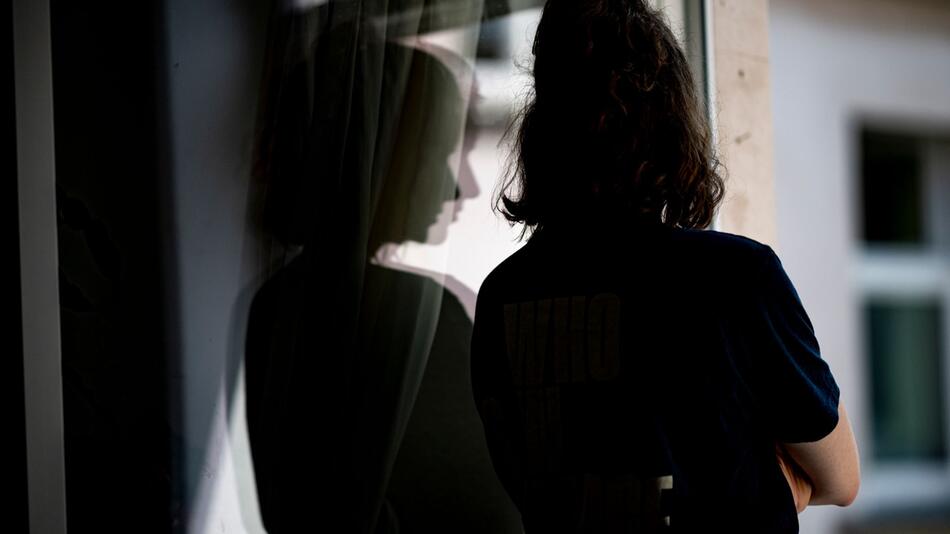 Junge Frau steht in einer Wohnung am Fenster