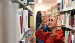 Frau steht wütend vor einem Bücherregal in der Unibibliothek