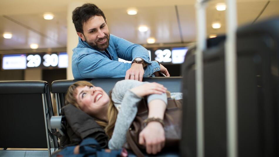 Ein Mann weckt eine Frau im Wartebereich eines Flughafen