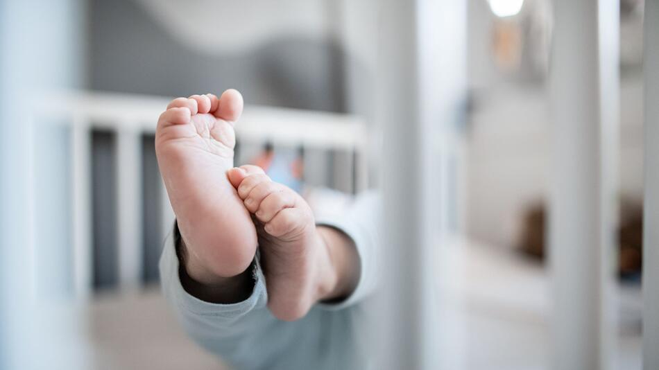 Die Füsse eines Babys in einem Kinderbett