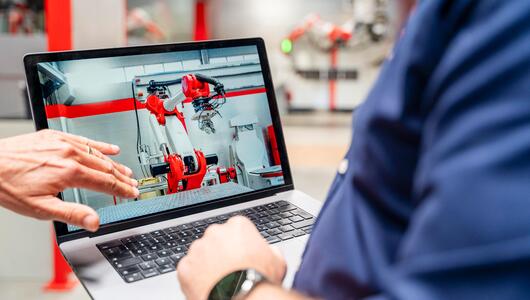 Beschäftigte betrachten auf einem Laptop die Steuerung eines Industrieroboters.