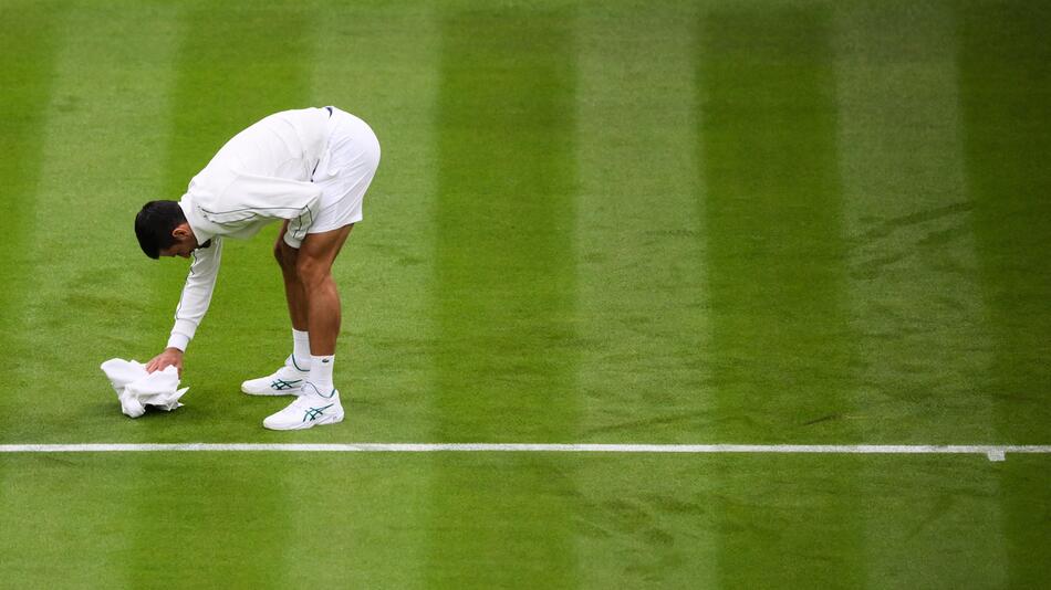 Novak Djokovic versucht am 3. Juli 2023 in Wimbledon, den Rasen mit einem Handtuch zu trocknen