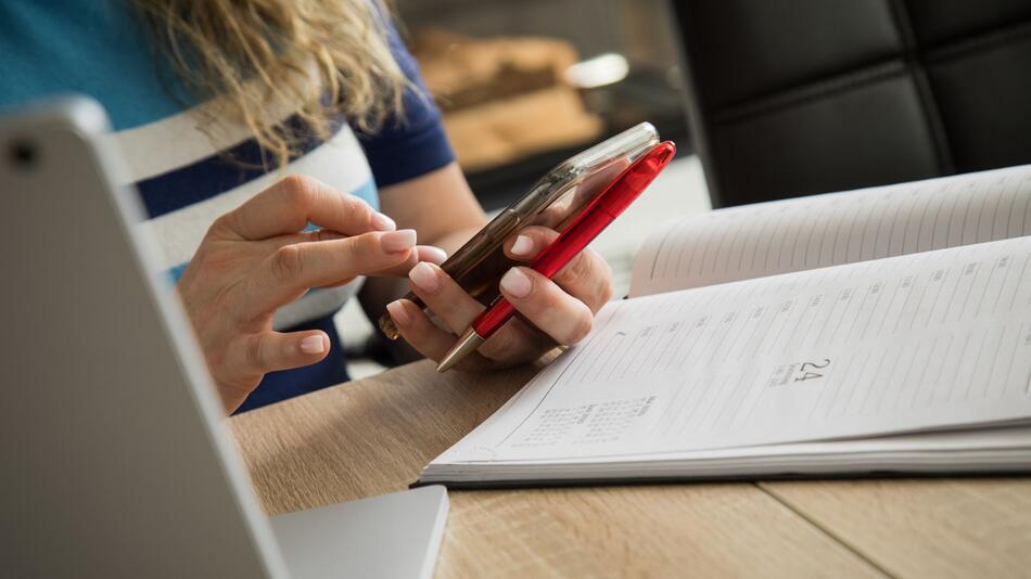 Frau schaut an ihrem Schreibtisch auf ein Smartphone