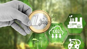 Hand hält eine 1-Euro-Münze vor einem unscharfen grünen Hintergrund, umgeben von grünen ...