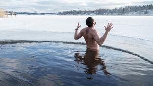 Ein Mann steht bis zur Taille in einem kreisrunden Loch im zugefrorenen See, umgeben von Eis und ...