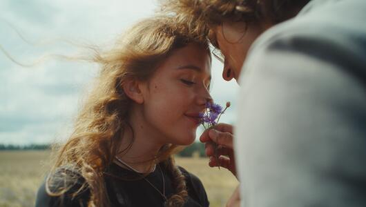 Junges Paar, er hält er ihr eine Blume unter die Nase, sie schnuppert daran. 