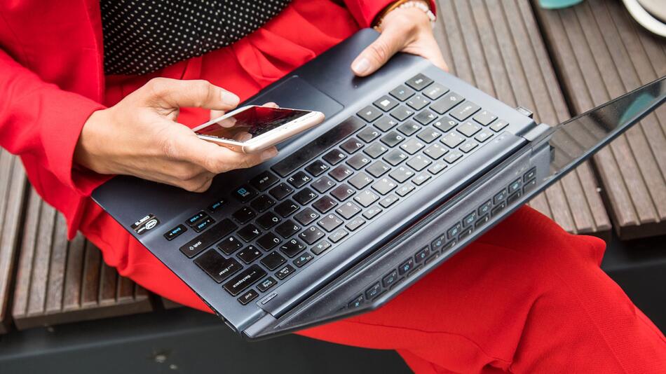 Eine Frau sitzt mit Smartphone und Laptop auf einer Bank
