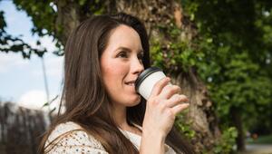 Eine Frau trinkt in einem Park Kaffee aus einem Einwegbecher