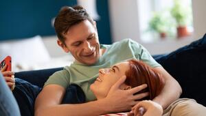 Eine Frau liegt auf dem Sofa auf dem Schoss ihres Mannes und lächelt ihn an.