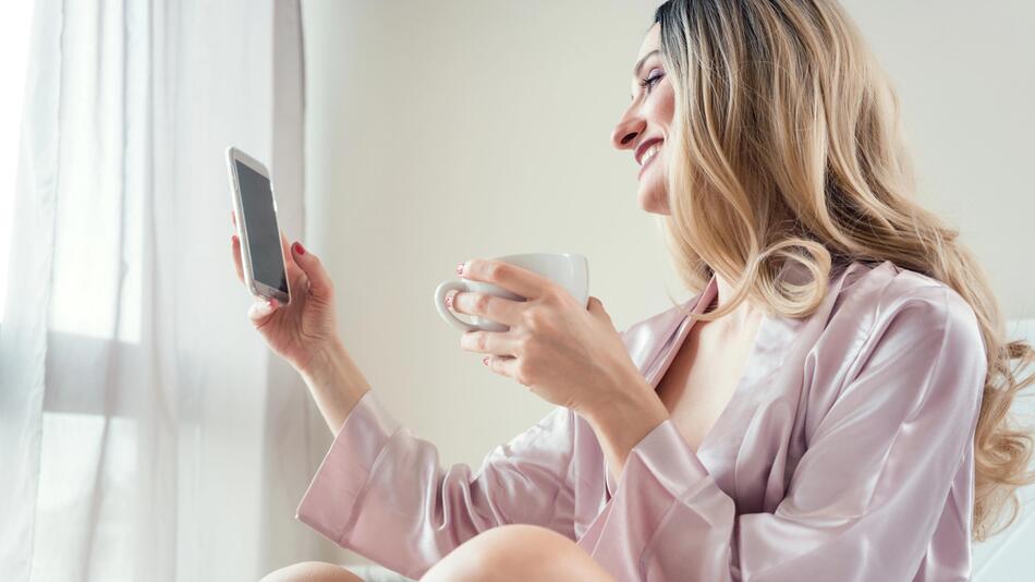 Frau im Bett mit Smartphone in der Hand