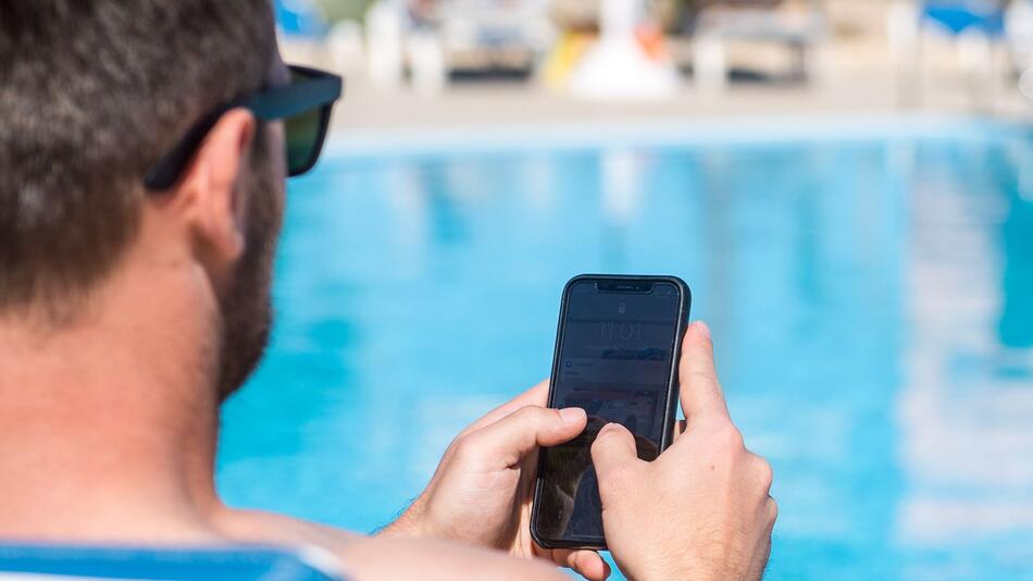 Mann mit Handy am Hotelpool