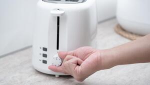 Eine Hand dreht an dem Regler eines weissen Toasters.