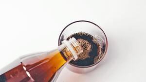 Eine braune Flasche giesst eine dunkle, kohlensäurehaltige Flüssigkeit in ein durchsichtiges Glas ...