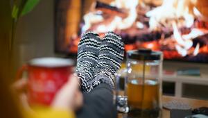 Gestrickte, schwarz-weiss gemusterte Haussocken an ausgestreckten Beinen vor einem flackernden ...