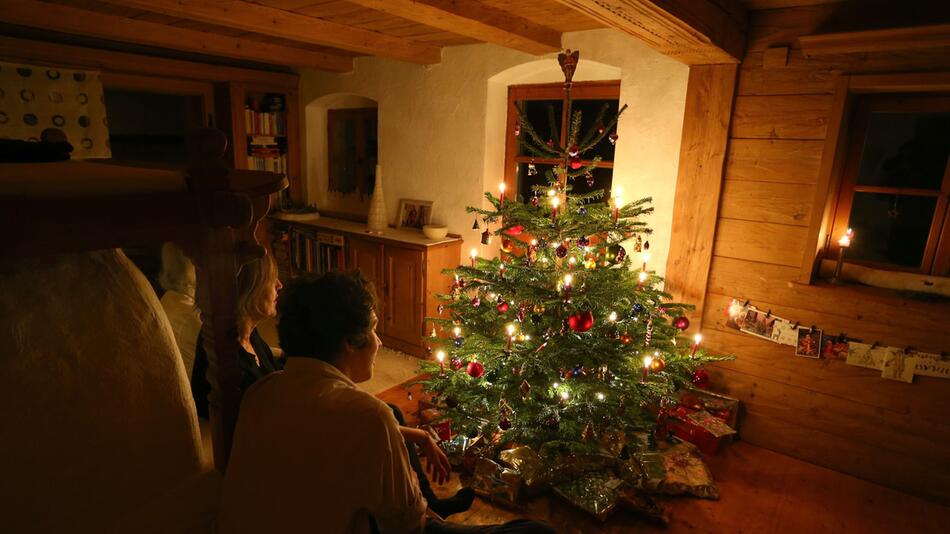 Familie sitzt vor einem beleuchteten Weihnachtsbaum