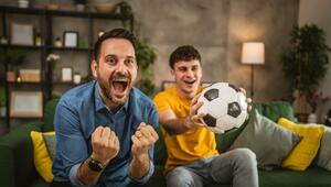Zwei Männer mit Fussball jubeln vor dem Fernseher 