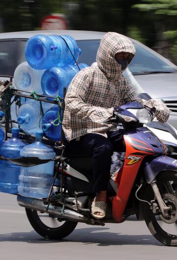 Mann fährt in Vietnam Kanister mit Wasser auf dem Roller. Er schützt sich mit langen Sachen.