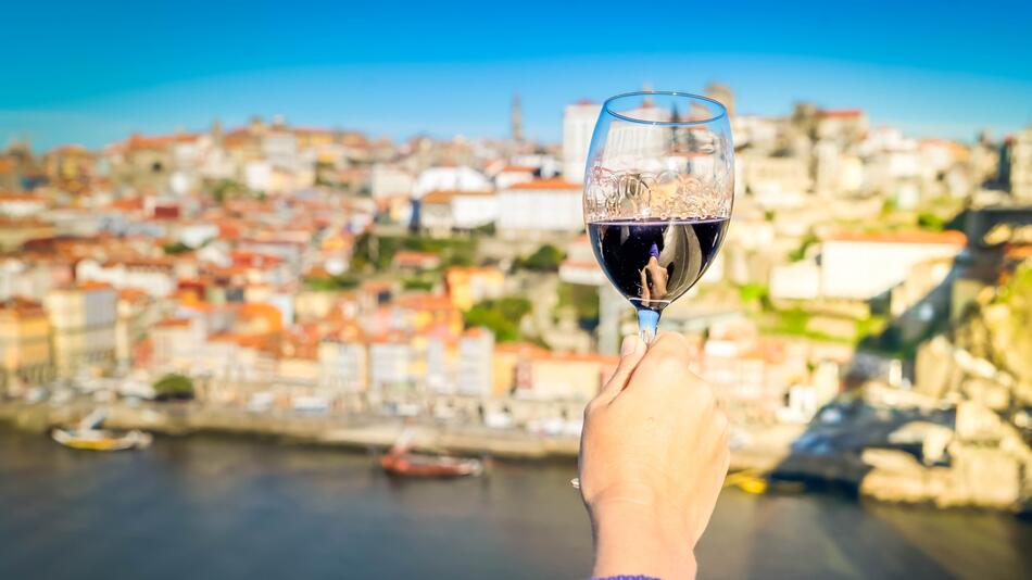Person trinkt am Fluss Douro ein Glas Wein