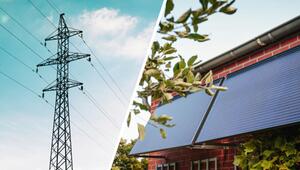 Links ein Strommast vor blauem Himmel, rechts Solarpaneele an der Fassade eines roten ...