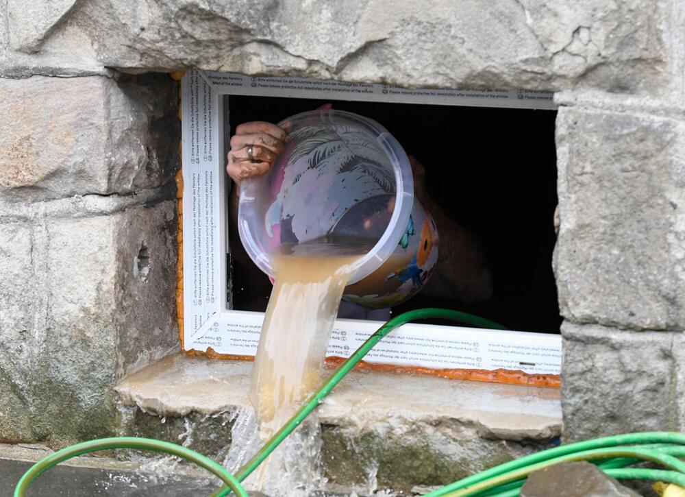 Wasser wird nach Überflutung aus einem Kellerfenster geschüttet