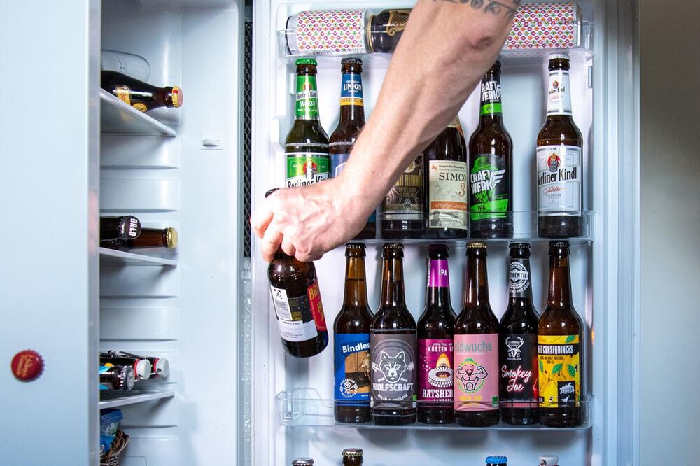Ein Mann entnimmt ein Bier aus einem Kühlschrank