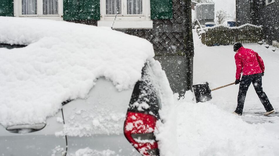 Eine Frau räumt Neuschnee aus der Zufahrt zu einem Haus