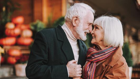 Paar mit grauen Haaren, das sich umarmt und nah zusammen steht. 