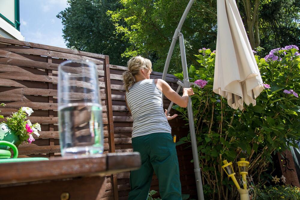 Eine Frau hantiert an einem Sonnenschirm herum