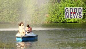 Zwei Frauen sitzen auf einem blauen Tretboot auf einem See, umgeben von grünem Laub. Eine Frau ...