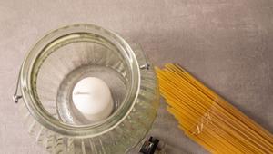 Spaghetti liegen neben einer Kerze in einem hohen Glas