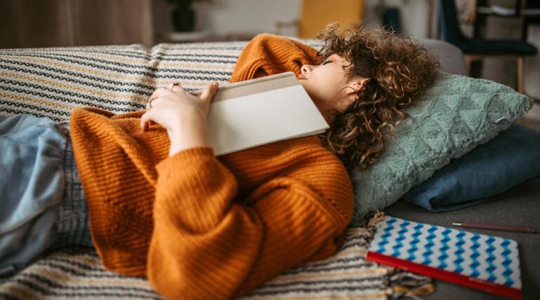 Frau schläft mit Buch auf sich liegend