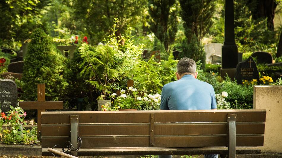 Ein Mann sitzt auf einer Friedhofsbank