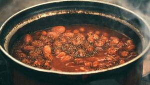 Ein Topf mit dampfenden, in Tomatensauce gekochten Bohnen, gewürzt mit Kräutern und Gewürzen.