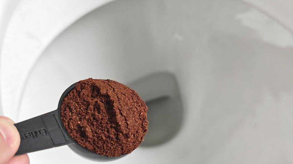 Löffel Kaffeesatz ist über einer Toilette zu sehen