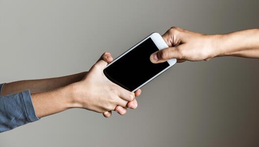 Kind klammert sich an ein Smartphone, das eine erwachsene Person aus der Hand nehmen möchte