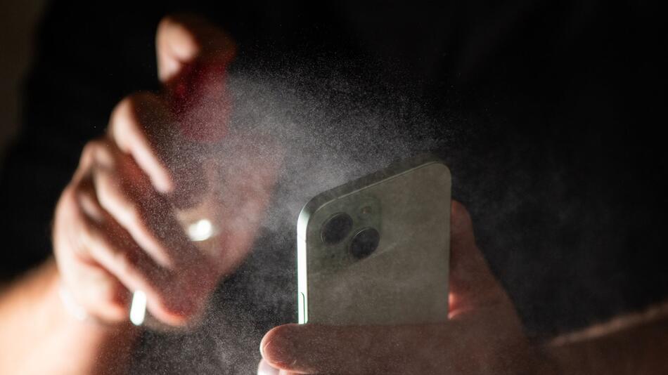 Mann reinigt sein Smartphone mit einem Spray