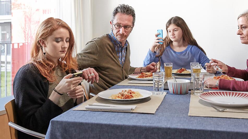 Familie am Esstisch, Kinder starren auf ihre Smartphones.