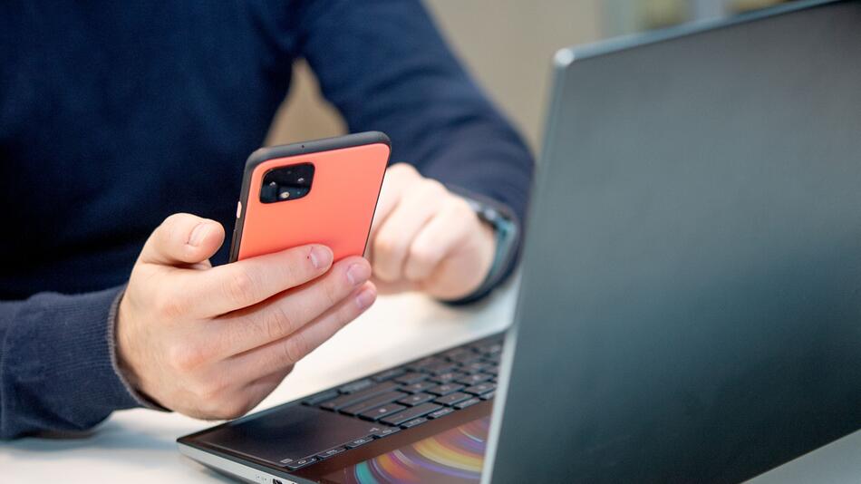 Ein Mann nutzt ein Handy am Laptop