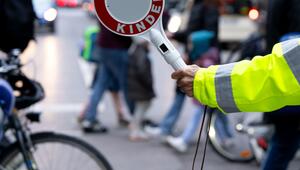 Eine Schulweghelferin steht mit einer Kelle vor einer Grundschule