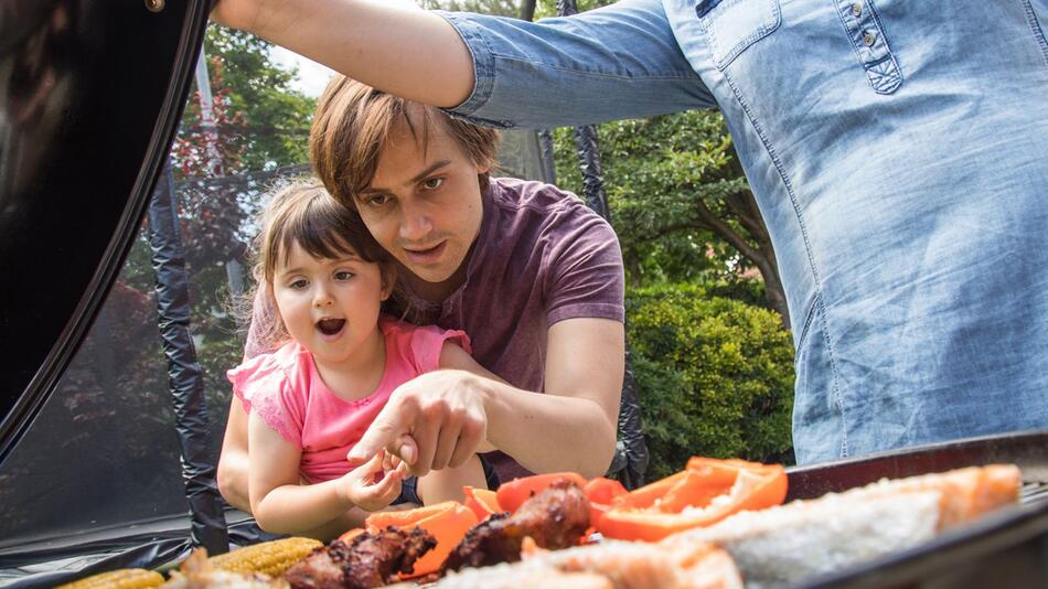 Familie mit Kleinkind grillt im Garten